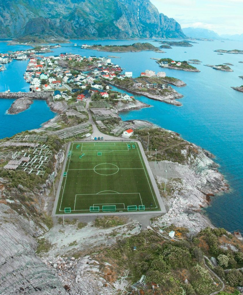 A breathtaking aerial view of a soccer field in Lofoten Islands, Vågan, Norway surrounded by stunning seascape and mountains.